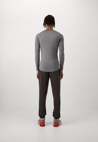 Person with braided hair wearing a fitted long-sleeve gray shirt, black sweatpants, and gray and red sneakers standing facing away.