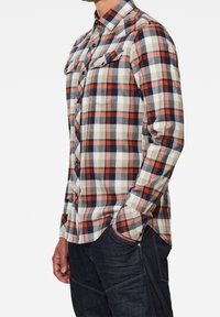 Rutigt flanellskjorta i kräm, orange, marinblå och grå färger; har bröstfickor, knappstängning och långa ärmar.