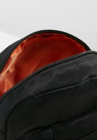 Czarny plecak z zamkiem błyskawicznym, z pomarańczową podszewką wewnątrz i gładką teksturą. Zewnętrzny materiał wydaje się trwały i solidny.