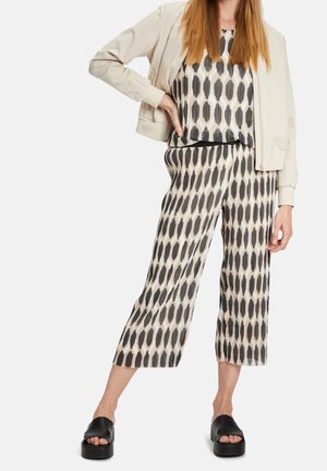 Femme portant une veste beige, un haut à motif noir et blanc et un pantalon large raccourci, associé à des mules plateformes noires.