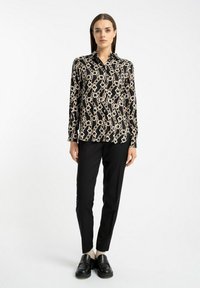 Czarna koszula zapinana na guziki z beżowym wzorem łańcuchów, z długimi rękawami i kołnierzem typu spread, w zestawieniu z dopasowanymi czarnymi spodniami i masywnymi czarnymi butami.