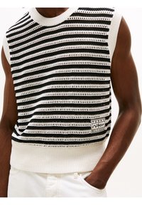 Bezrekawnikowy dziany sweter z czarno-białymi poziomymi paskami, z teksturowanymi wzorami ażurowymi oraz naszywką z logo na brzegu.
