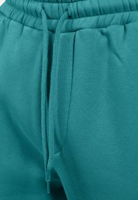 Teal joggerbroek gemaakt van zachte, stretchy stof. Voorzien van een elastische tailleband met trekkoorden en zijzakken. Soepele textuur.