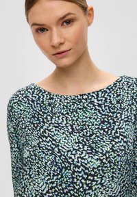 Dunkles, gemustertes Oberteil mit einem wellenförmigen Design in Grün und Weiß auf einem marineblauen Hintergrund, mit einem runden Ausschnitt und weicher Textur.