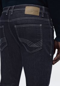 Σκούρα μπλε τζιν με λευκή ραφή, πίσω τσέπες με διακοσμητικές ραφές και καφέ δερμάτινο ταμπελάκι με την ένδειξη "Tom Tailor" στη μέση.