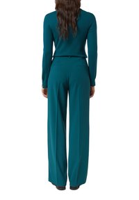 Turkusowy dzianinowy sweter z długimi rękawami w zestawieniu z wysokim stanem i szerokimi nogawkami spodni. Spodnie mają boczne kieszenie i gładką fakturę.