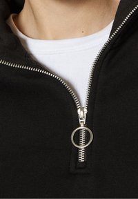Svart ziphoodie med silverdragkedja och ringdragknapp, lager över en vit t-shirt med rund halsringning och ribbad textur.