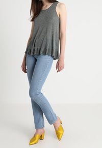 Grå ärmlös topp med en utställd fåll, matchad med ljusblå tighta jeans och klara gula spetsiga klackar. Släta texturer genomgående.