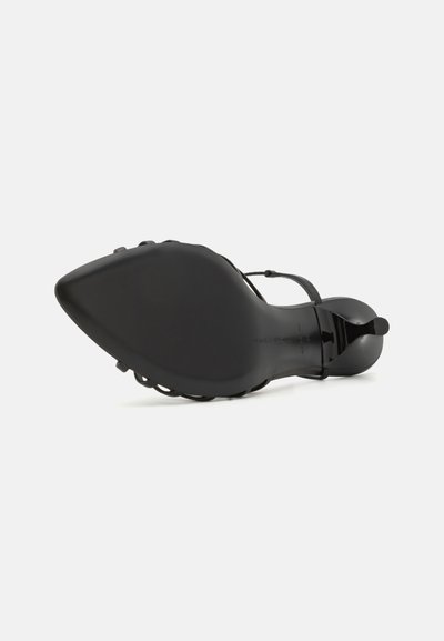 Sort højhælet sko med spids tå, glat tekstur og tynd ankelrem. Har et udskåret design og en slank, blank finish.
