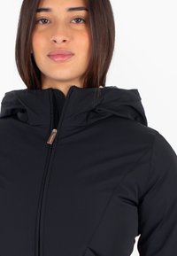Giacca nera con zip e cappuccio, caratterizzata da una texture liscia e opaca e da un design elegante. Comprende un piccolo accento in metallo sulla zip.