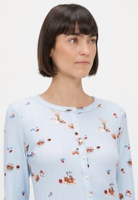 Svijetloplavi rebrasti majica s dugim rukavima koja ima prednje kopčanje, s uzorkom kolačića, kave i cvijeća u raznim bojama.