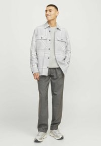 Chaqueta de camisa a cuadros grises con botones a presión sobre un suéter gris claro, combinada con pantalones gris oscuro y zapatillas plateadas.