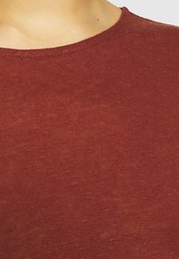 Röd stickad skjorta med rund halsringning. Tyget har en texturerad yta, med subtila färgvariationer och en mjuk känsla.