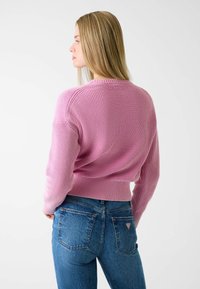 Pink ribbed sweater with a round neckline and fitted hem, paired with blue high-waisted jeans featuring a logo patch on the back.