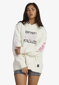 Cream hoodie with graphic text and designs in black and light pink. Features a kangaroo pocket and ribbed cuffs, paired with striped shorts.