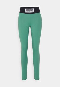 Leggings verdi con una texture liscia e una vita nera con logo. Il design è aderente e presenta una silhouette a lunghezza completa.