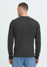 Mørkegrå tekstureret striktrøje med lange ærmer, ribbede manchetter og kant. Bærendes med lyse, løstsiddende denim jeans.