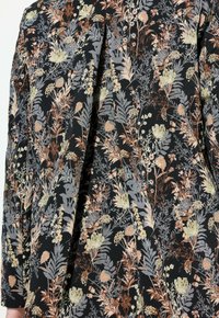 Mustalla kankaalla on kukkakuosi, jossa on hillittyjä vihreän, persikan ja hopean sävyjä. Suunnittelussa on monenlaisia kasvin muotoja ja tekstuureja.