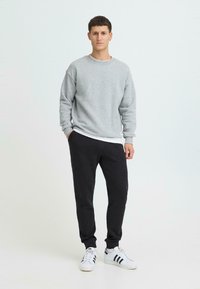 Szara bluza z długimi rękawami, zestawiona z ciemnymi dresami i białymi trampkami z czarnymi paskami. Casualowy, sportowy strój.