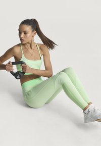 Lichtgroene sportoutfit bestaande uit een geribbelde crop top en high-waisted legging met gestreepte panelen. Het model houdt een zwarte kettlebell vast.