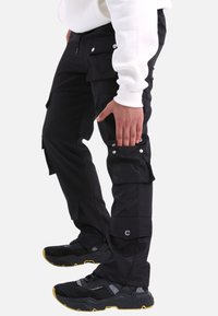 Schwarze Cargo-Hosen mit mehreren Seitentaschen, Druckknöpfen und schmalem Schnitt. Hergestellt aus strapazierfähigem Material mit einer glatten Textur.