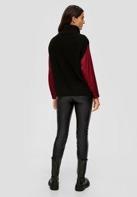 Pull en col roulé noir à côtes, superposé à une blouse bordeaux avec des manches boutonnées, associé à un pantalon noir ajusté et des bottes noires.