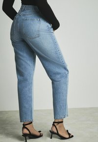 Jean taille haute bleu clair avec une coupe droite, comportant deux poches arrière et des ourlets, associés à des sandales à talons noires à lanières.