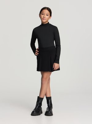 Top nero a maniche lunghe abbinato a una gonna nera svasata e stivali neri alla caviglia. L'outfit presenta una silhouette aderente e una texture liscia.