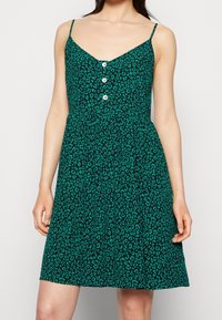 Vestido verde con estampado de leopardo, tirantes finos, escote en V y un detalle de botones en la parte delantera. Confeccionado en una tela ligera con una silueta fluida.