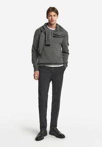 Grauer Strickpullover mit rundem Halsausschnitt, kombiniert mit einem passenden Schal, dazu schwarze Hose und schwarze Schnürschuhe.