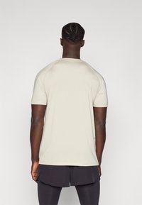 Beige kortermet treningstrøye med rund hals og raglanermer, med en glatt tekstur og minimalistisk design.