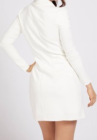 Robe blanche à manches longues avec une silhouette ajustée, dotée d'un col et d'une texture lisse. Vue de dos montrant un ourlet droit et des coutures simples.