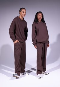 Sudadera grande marrón y pantalones a juego hechos de una tela suave. Ambos conjuntos tienen un corte relajado y detalles de diseño minimalistas.