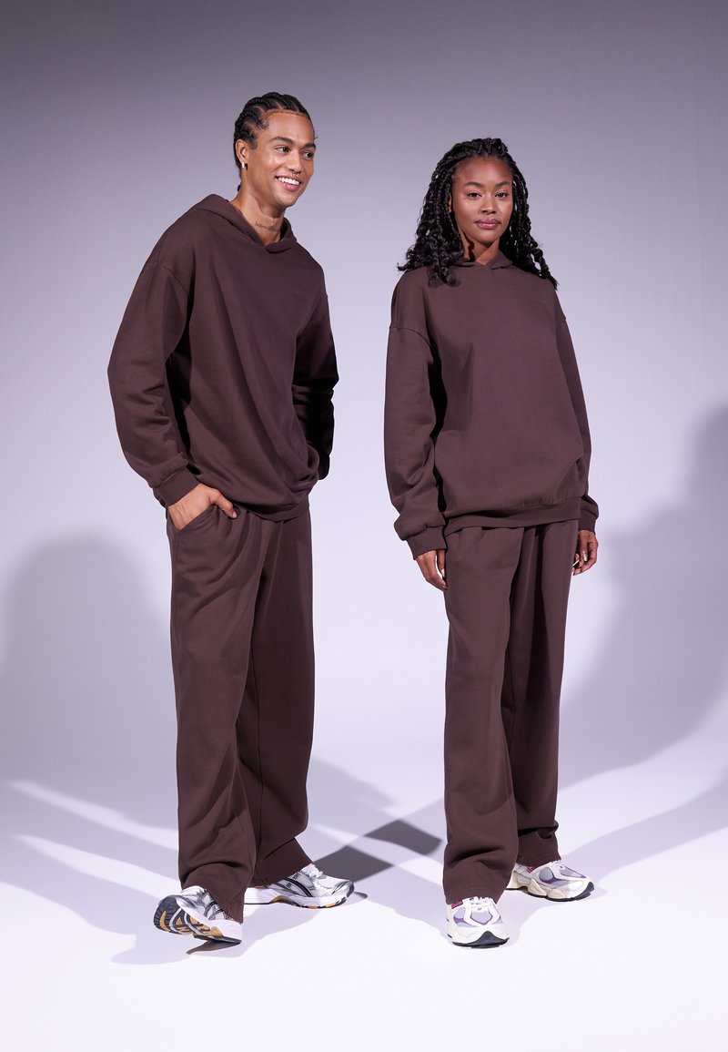 Sudadera grande marrón y pantalones a juego hechos de una tela suave. Ambos conjuntos tienen un corte relajado y detalles de diseño minimalistas.