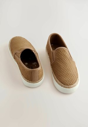 Hnedé tkané slip-on topánky s bielou gumovou podrážkou a pleteným lemovaním. Ploché, zaoblené špičky, otvorené bočné strany a žiadne viditeľné šnúrky.