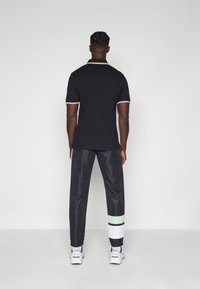 Čierne polo tričko s bielym a zlatým lemovaním, skombinované s čiernymi nohavicami s zelenými a bielymi pruhmi. Biele tenisky dopĺňajú outfit.