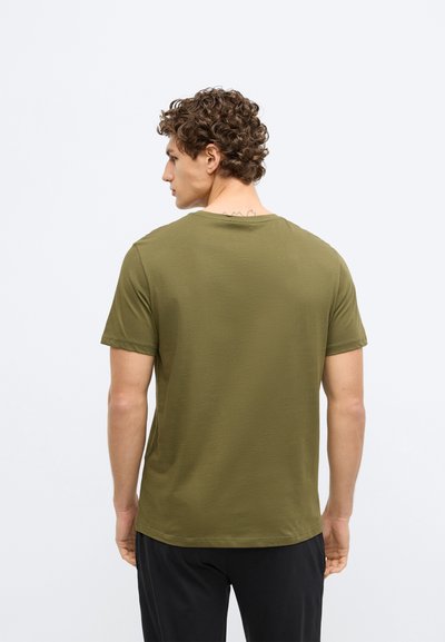 Ķiršu zaļas krāsas īsām piedurknēm T-krekls no mīksta kokvilnas auduma. Tam ir klasiskas apļveida apkakles izgriezums un brīvs piegriezums, gluda tekstūra un nav redzamu rakstu.