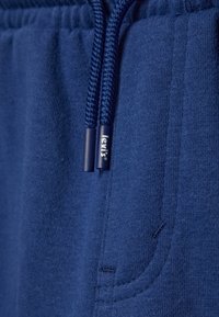 Námořnická modrá mikina s měkkou texturou, vybavená stahovací šňůrkou a boční kapsou. Na štítku značky je napsáno "Levi's."