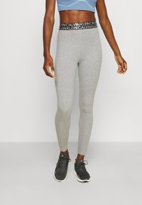 Grå leggings med en sort Calvin Klein-logo i taljen, lavet af strækbart materiale. Sættes sammen med sorte træningssko.