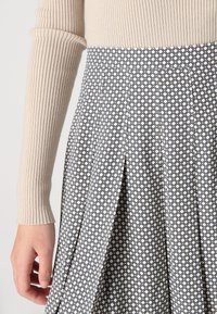 Beige ribbet langermet topp kombinert med en plisserte skjørt med et geometrisk mønster i marineblått og krem. Strukturert stoffdetalj synlig.