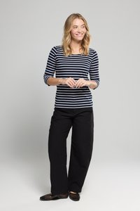 Marineblå og hvide stribede langærmede top, parret med sorte vidde bukser og sorte net-flade sko. Modellen står afslappet med hænderne foldet.