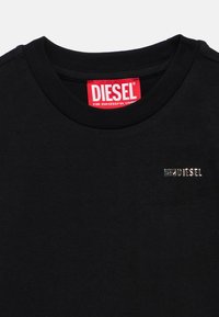 Μαύρο T-shirt με ριμπ λαιμόκοψη, με κόκκινη ετικέτα Diesel και μικρό ασημί λογότυπο Diesel μπροστά. Λείο βαμβακερό ύφασμα.