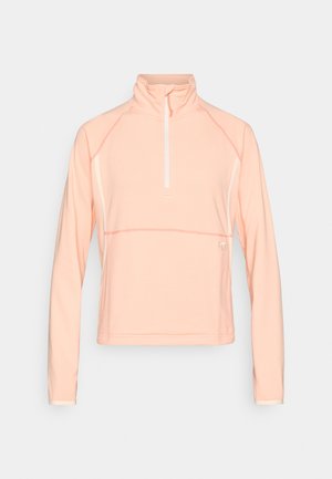 Light peach long-sleeve quarter-zip top made from textured fabric, featuring a high collar and contrasting white seams and accents.