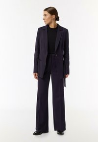 Navy tailored suit with a fitted blazer and wide-leg trousers. Smooth fabric, minimal detailing, and a single-button closure on the blazer.