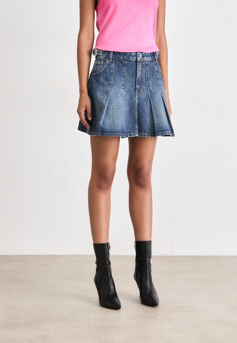 Fustă plisată din denim, de culoare albastru închis, fabricată dintr-un material texturat. Prezintă o talie ajustată cu închidere prin nasture. Este asortată cu botine negre.