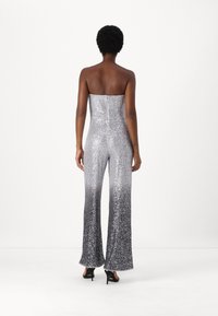 Sølv paljett jumpsuit med stroppeløst design, utsvingte ben og en ombre-effekt som går fra lys til mørk ved kanten.