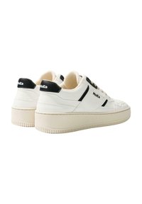 White sneakers with a textured surface, black accents at the heel and sides, and a chunky beige rubber sole. Features logo on the heel.