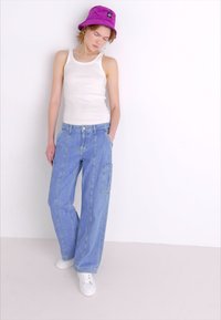 Vaaleansiniset farkkucargo-housut, joissa on väljä malli, kyljissä taskut ja litteä etuosa. Yhdistetty valkoisen toppauksen ja violetin ämpärihatun kanssa.