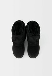 Bottes noires en matériau suédé, avec une manche en tricot côtelé, un bout rond et une doublure en peluche pour plus de chaleur. Les semelles en caoutchouc plat assurent une stabilité.