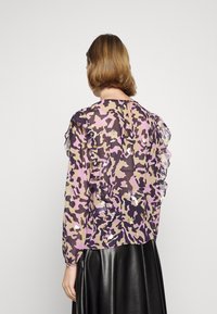 Durchsichtige Bluse mit einem Camouflage-Muster in Pink, Lila und Beige, mit Rüschen an den Ärmeln und einem Schlüsselrücken-Detail.